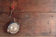 7964762-old-watch-hanging-on-fish-hook-with-red-thread-on-wooden-background.webp